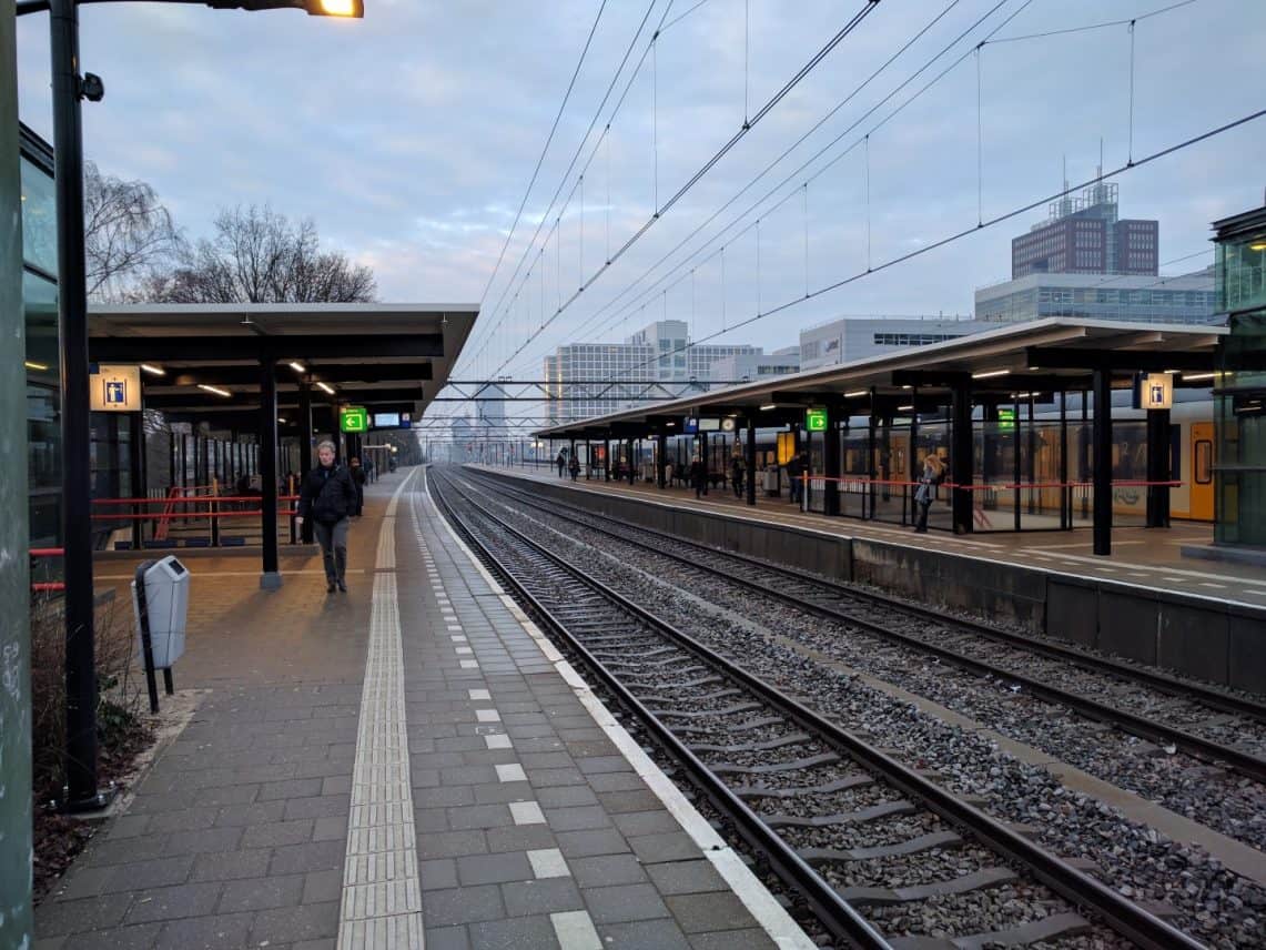 Een treinstation prachtig vastgelegd door de lens van een Kodak Ektra, met lege banken en een verre trein op de achtergrond.