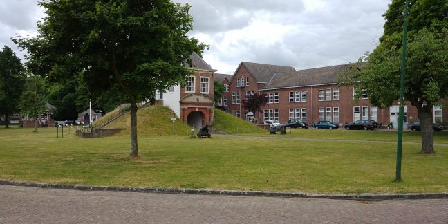 Een bakstenen gebouw omringd door een weelderig groen landschap, dat trots midden in de rust staat.