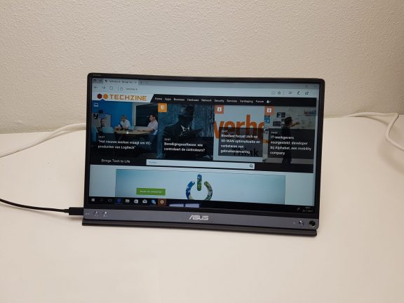 Een Asus ZenScreen MB16AC-laptop staat op een bureau met een oplader eraan.