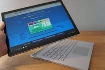 Een persoon houdt een Microsoft Surface Book 2 op een tafel.