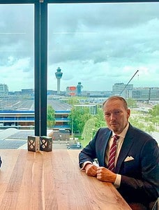 Twee mannen in pak zitten aan een tafel voor een raam.