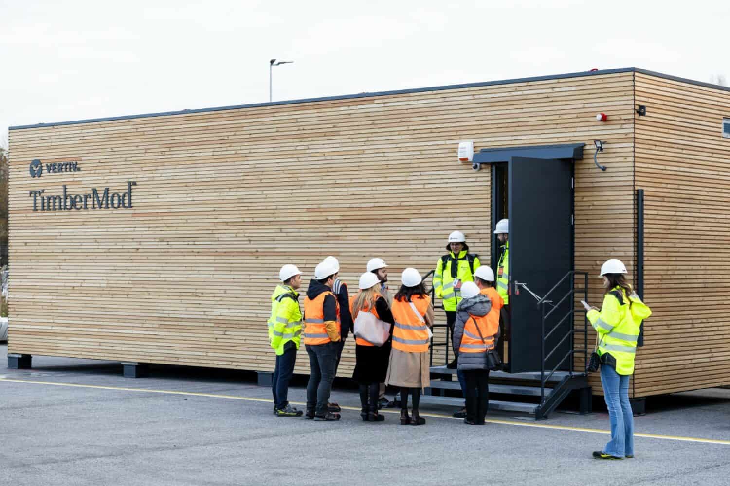 Een groep bouwvakkers staat voor een houten gebouw.