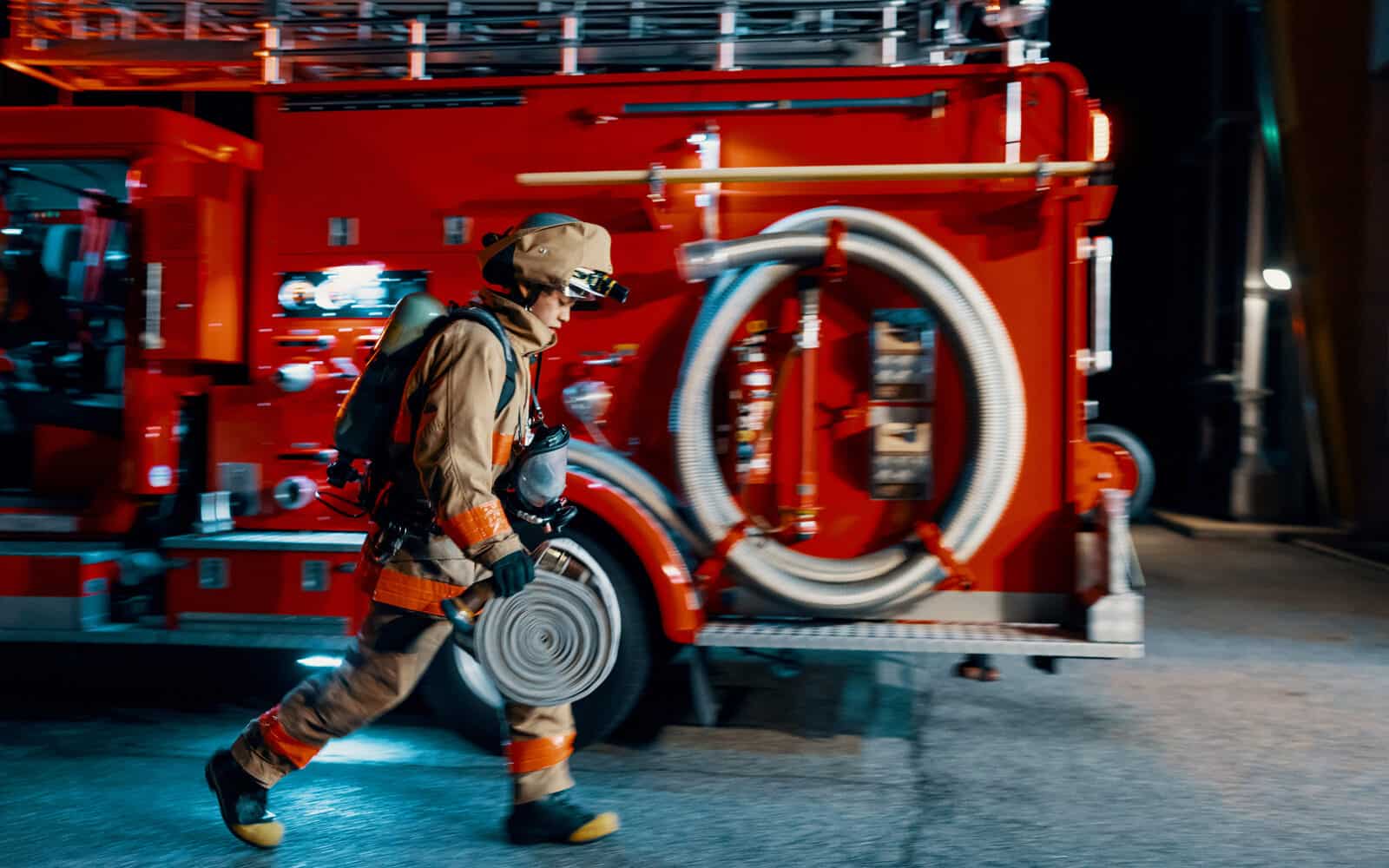 Een brandweerman die 's nachts voor een brandweerwagen loopt.