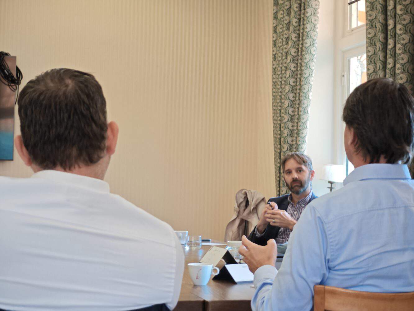 Een groep mensen die aan een tafel zitten en met elkaar praten.