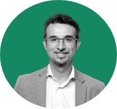 Een man met een bril en een jas op een groene achtergrond.