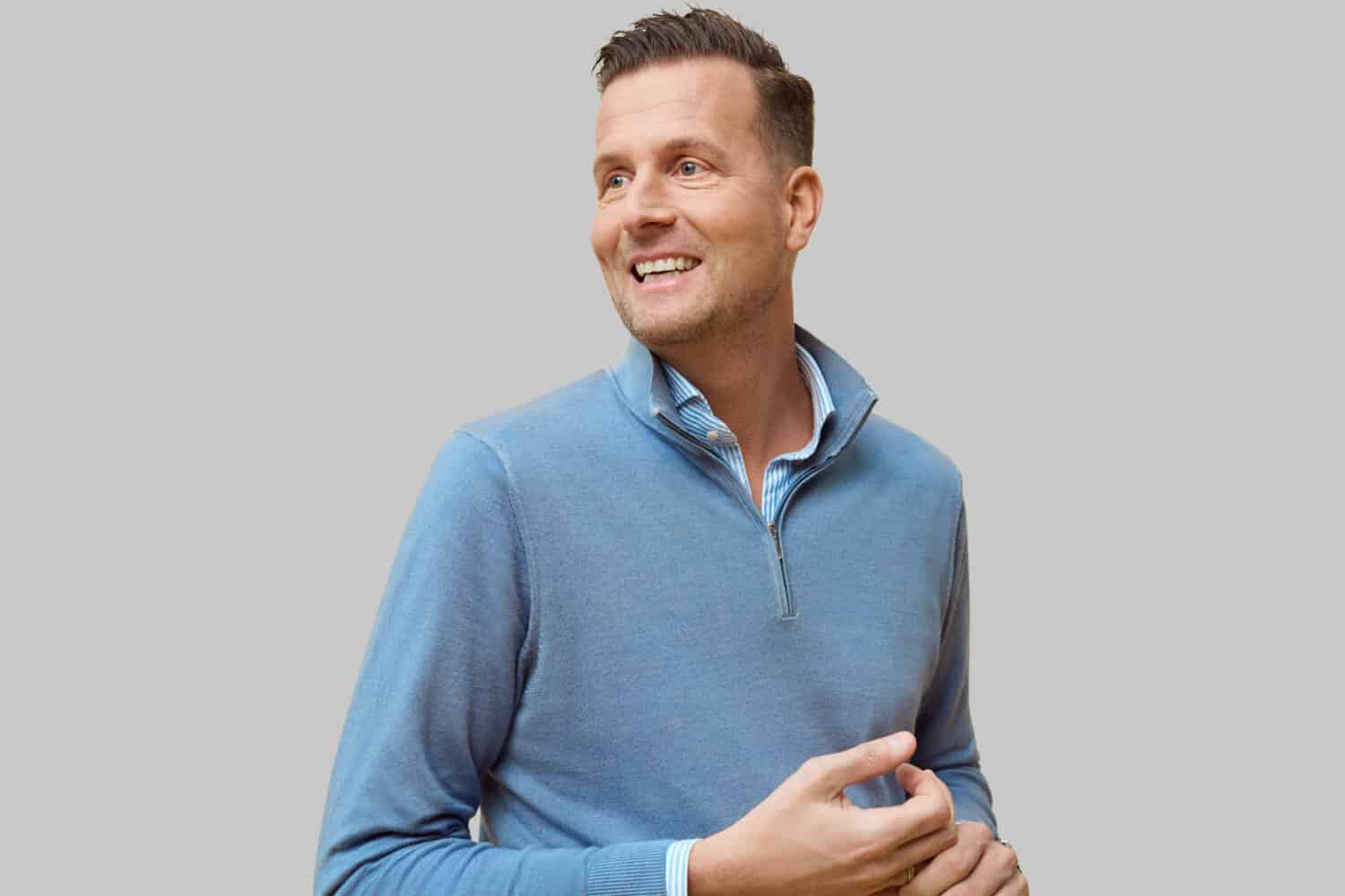 Een man in een blauwe trui lacht.