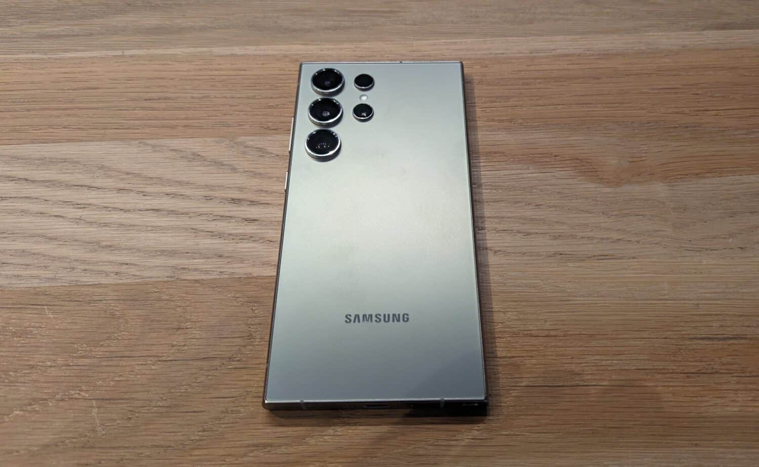 Een zilveren Samsung-telefoon op een houten tafel.