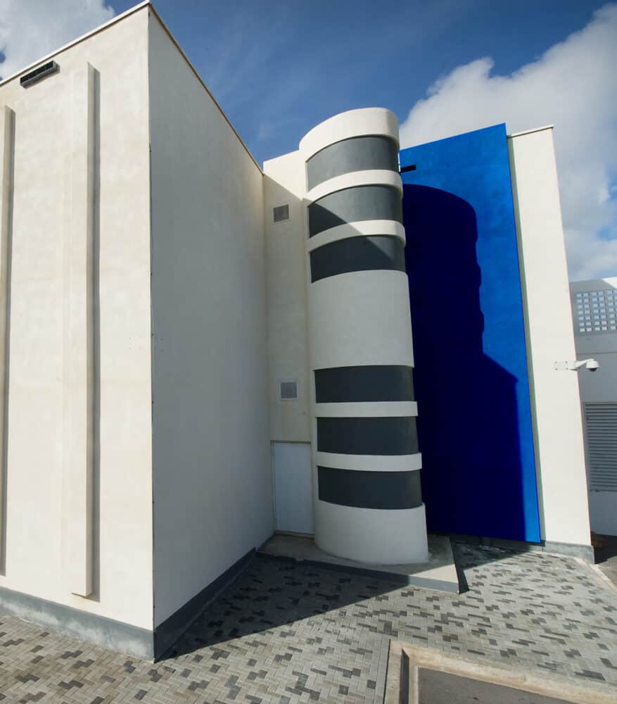 Moderne gevel van een gebouw met een cilindervormig element met horizontale strepen en een helderblauwe deur.