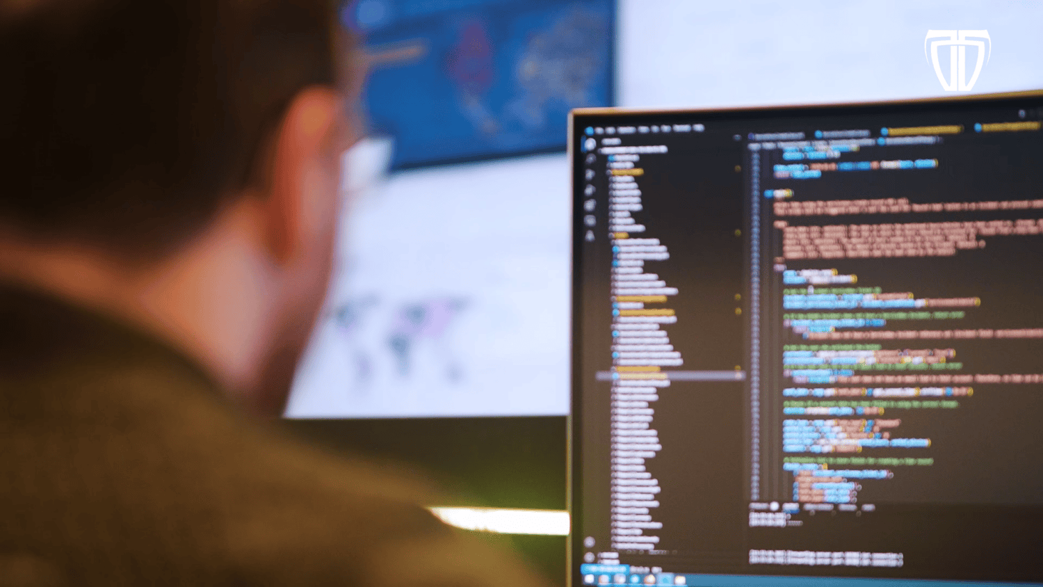 Een persoon die op een computer werkt met code op het scherm, onscherp op de voorgrond.