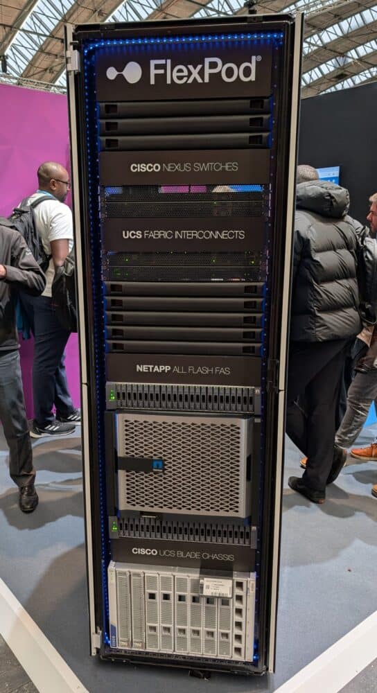 FlexPod-serverrack met Cisco Nexus-switches, UCS-fabric-interconnects, NetApp-opslag en UCS-bladechassis. Mensen staan rond de apparatuur.
