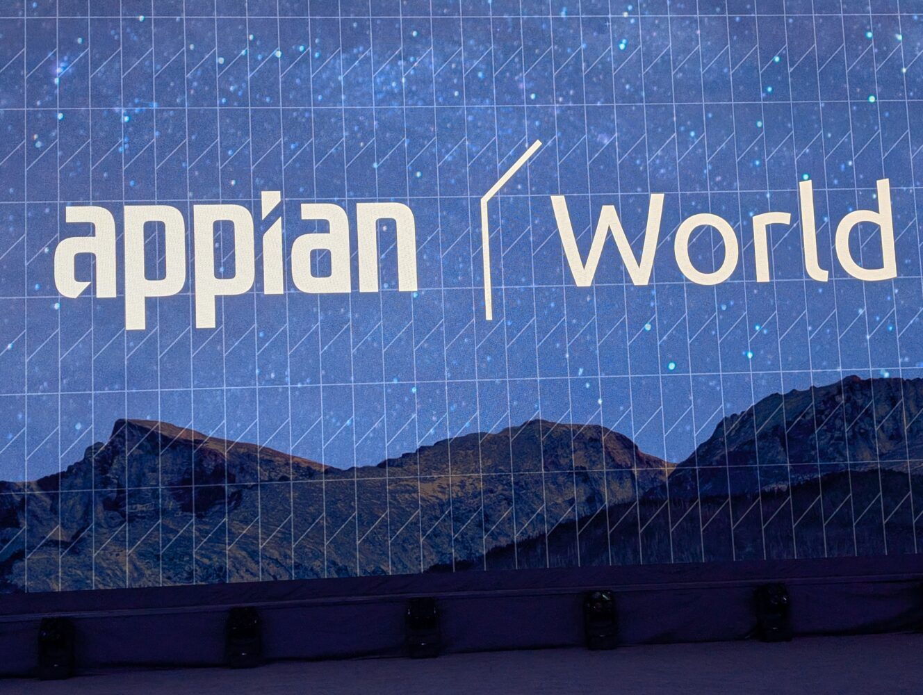Op een groot display staan de woorden "Appian World" met op de achtergrond het silhouet van een bergketen en een sterrenhemel.