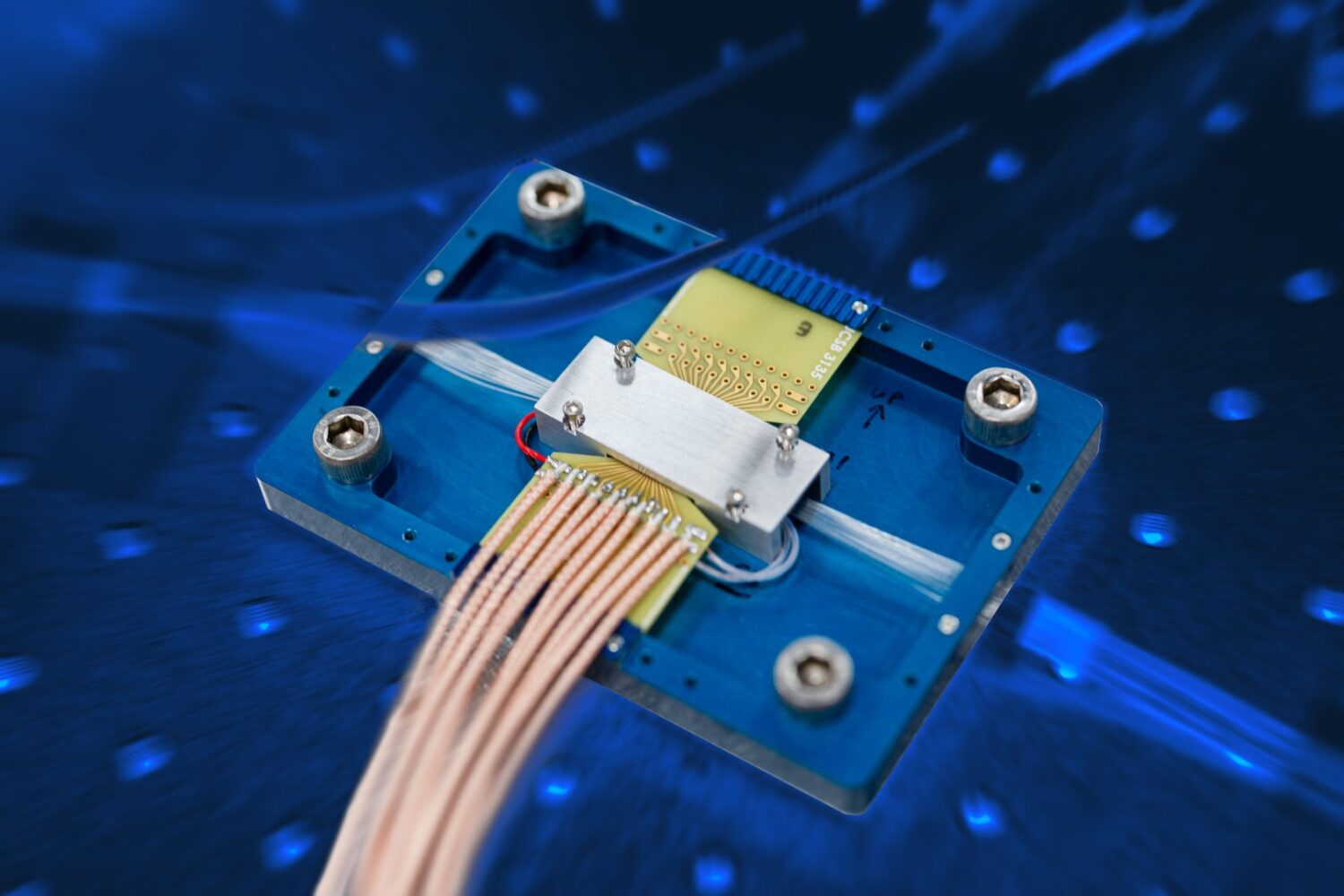 Cisco Newsroom Creative_Cisco Quantum Entanglement Source Chip_Back (Large) Close-up van een Quantum Network Entanglement Chip met meerdere verbonden draden, gemonteerd op een blauwe metalen basis tegen een wazig blauwe achtergrond.