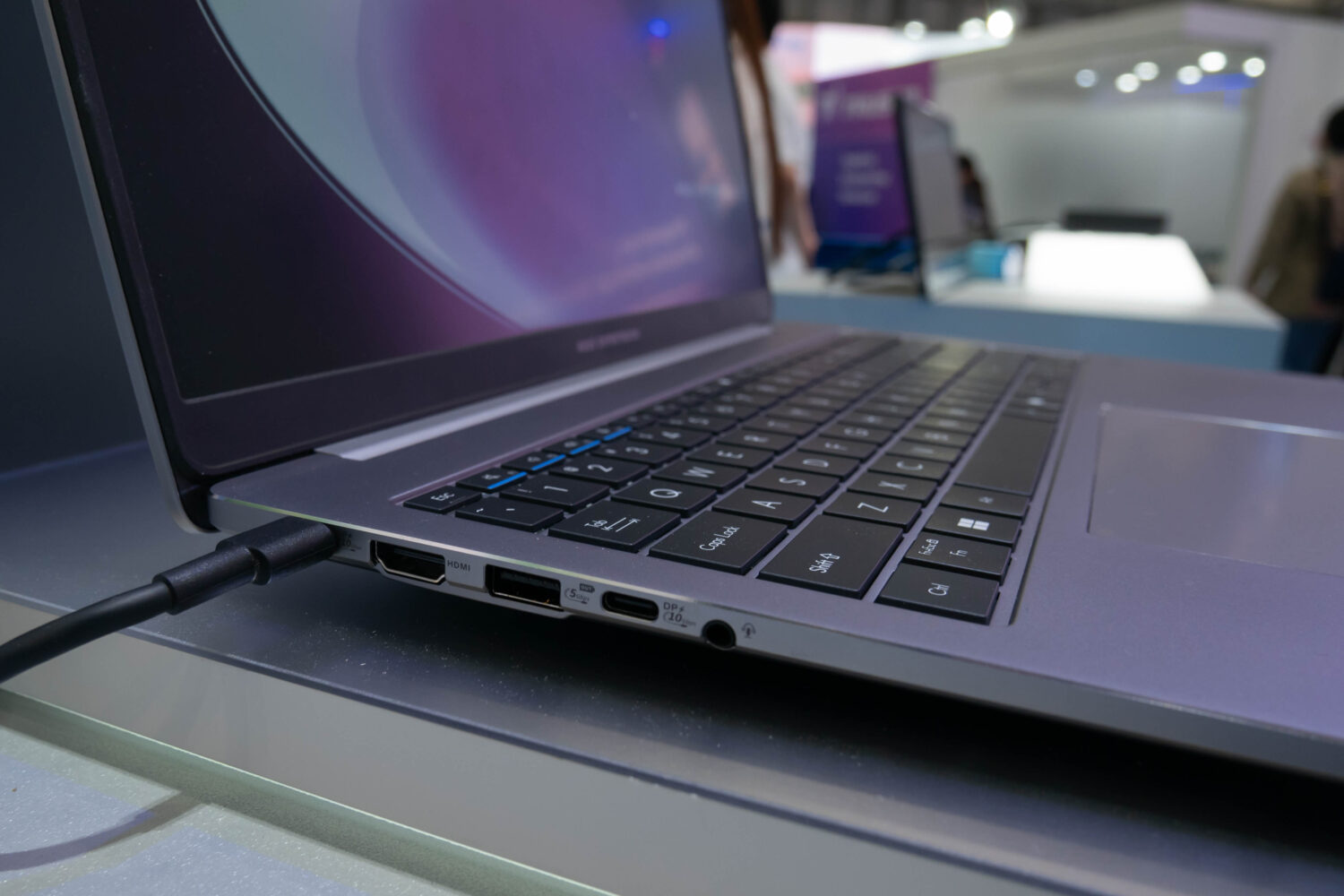 Een close-up van de linkerkant van een laptop met de aansluitingen voor HDMI, USB, een koptelefoonaansluiting en de rand van het toetsenbord. De laptop is aangesloten en staat op een tafel met een beeldscherm.