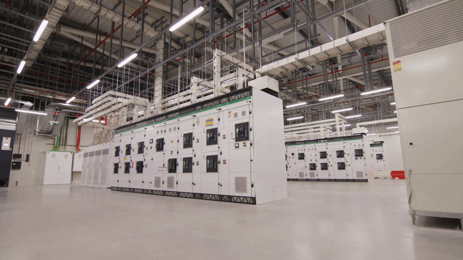 Start Campus_Schneider Electric 3 (Large) Grote elektrische schakelpanelen staan in rijen opgesteld in een ruim industrieel pand, met blootliggende bedrading en leidingen boven zich.
