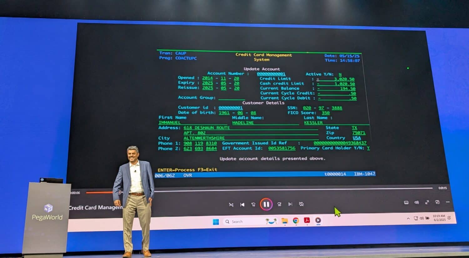 Een man staat op het podium naast een groot scherm met een groen-zwarte mainframe-interface voor een creditcardbeheersysteem, en belicht Pega Blueprint tijdens een PegaWorld-evenement.