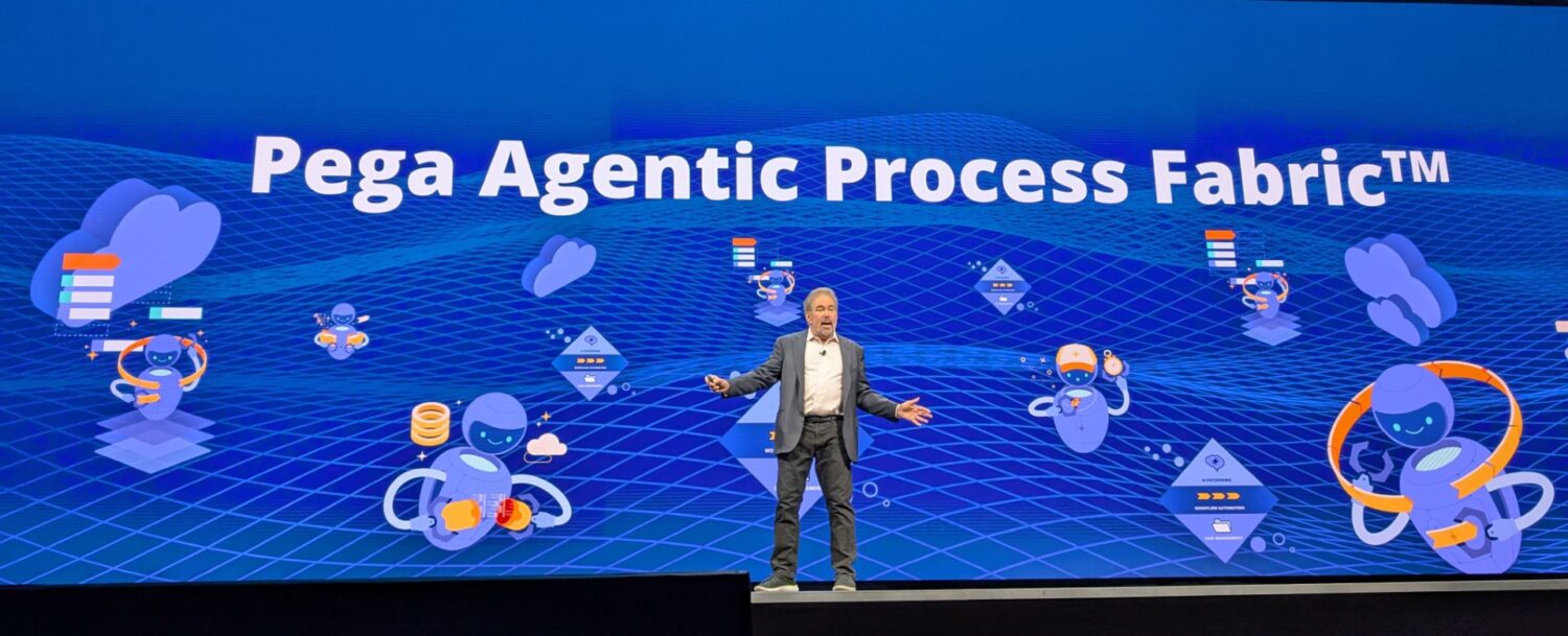 Een persoon in zakelijke kleding staat op het podium voor een blauw scherm met daarop "Pega Agentic Process Fabric™", verschillende technologische afbeeldingen en verwijzingen naar Pega Blueprint.
