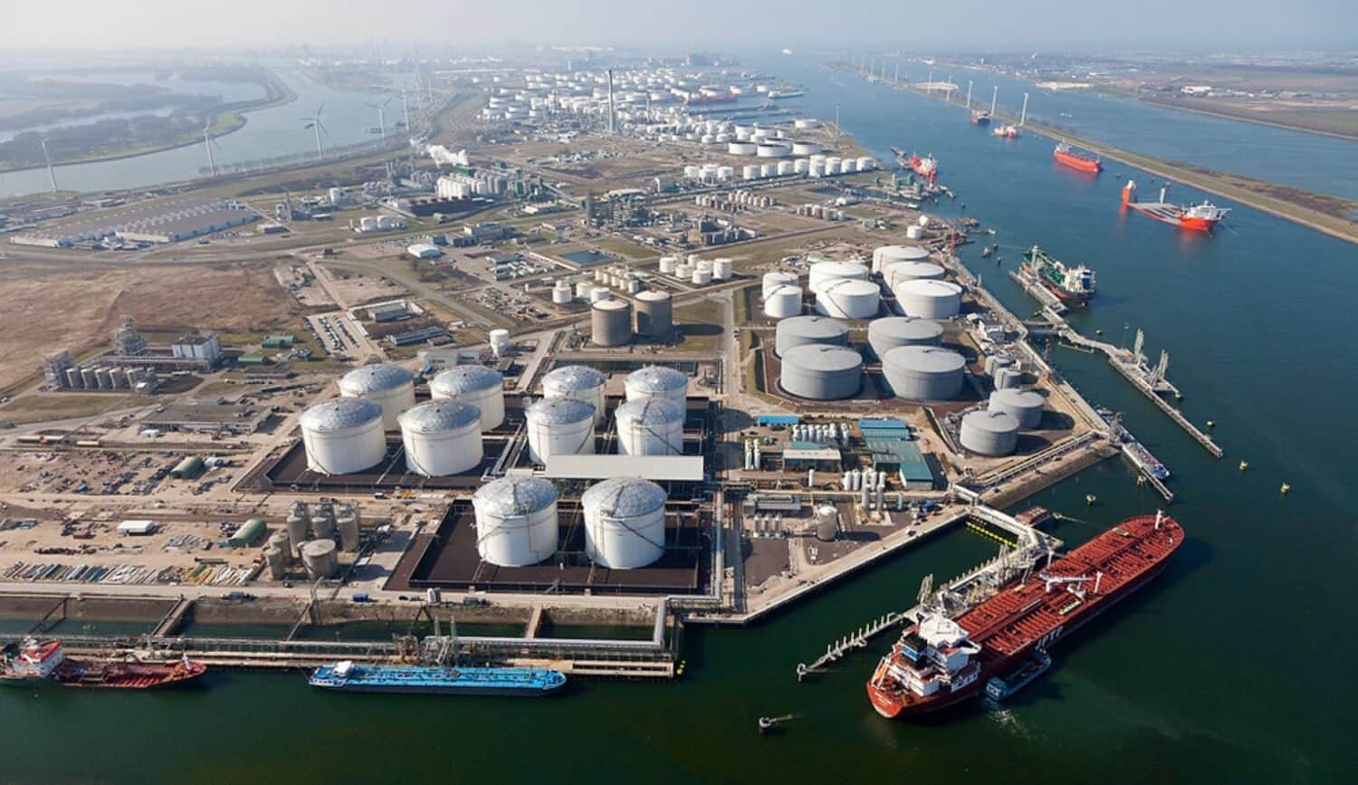VTTI_1 (Large) Luchtfoto van een grote industriële haven met olieopslagtanks, aangemeerde vrachtschepen, pijpleidingen en waterkanalen.