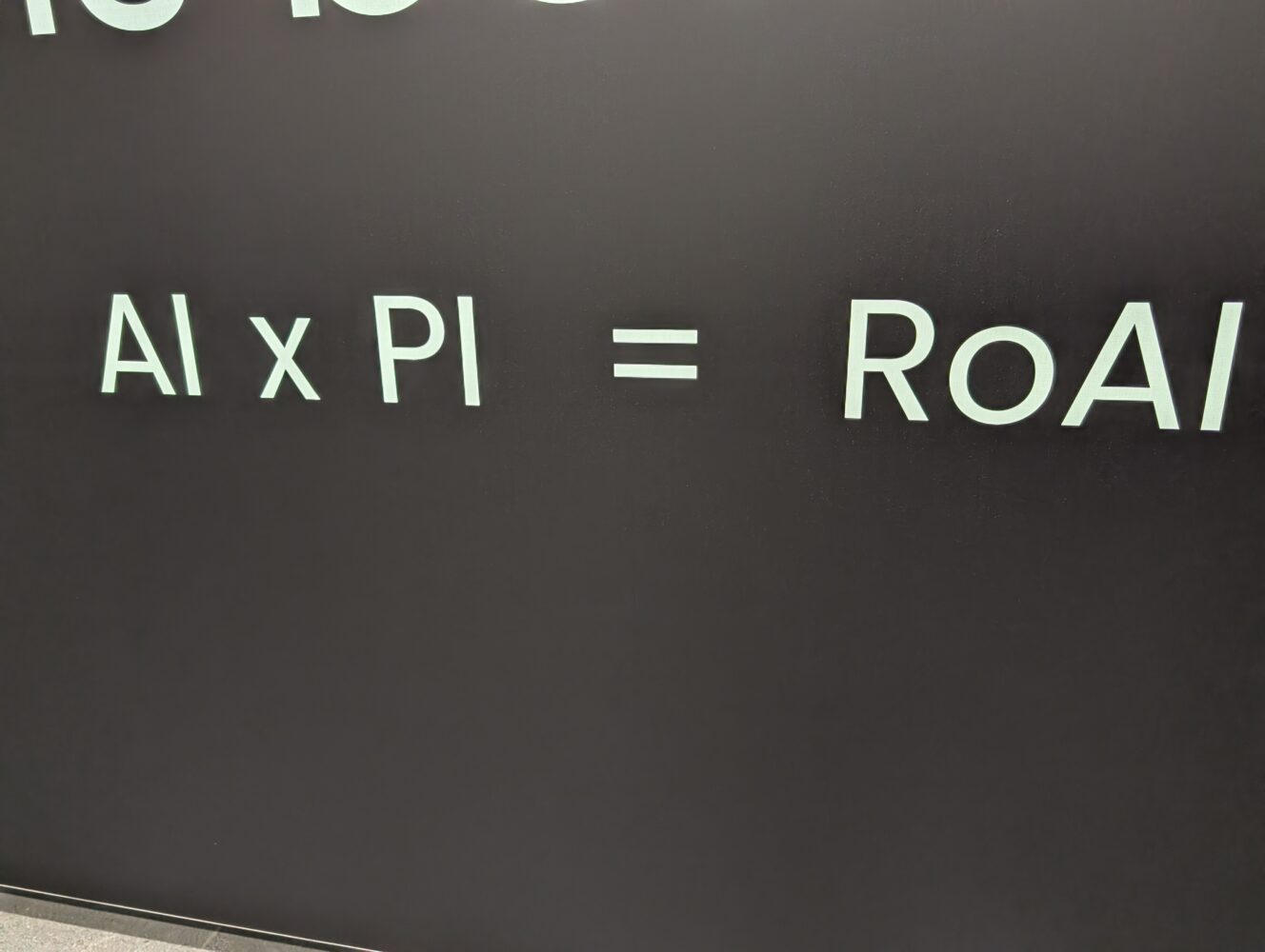 Op een zwarte muur staat in grote, lichtgekleurde letters "AI x PI = RoAI".