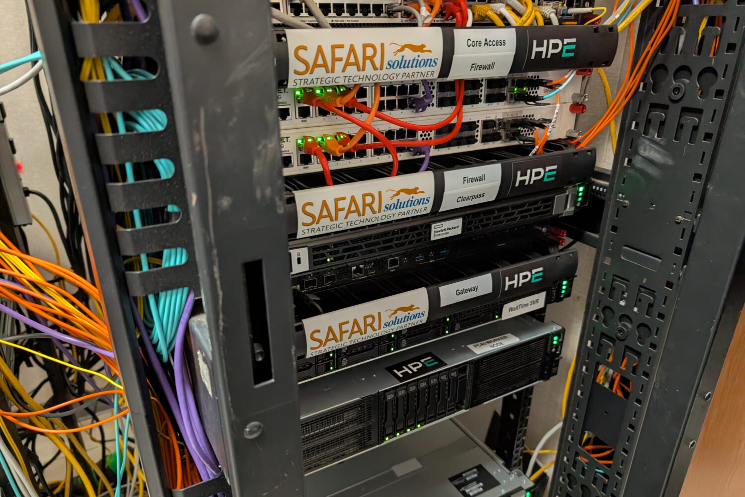 Rack_Ryder_Cup Een serverrack met meerdere netwerkapparaten en kabels van HPE en Safari Solutions, met brandende indicatielampjes.