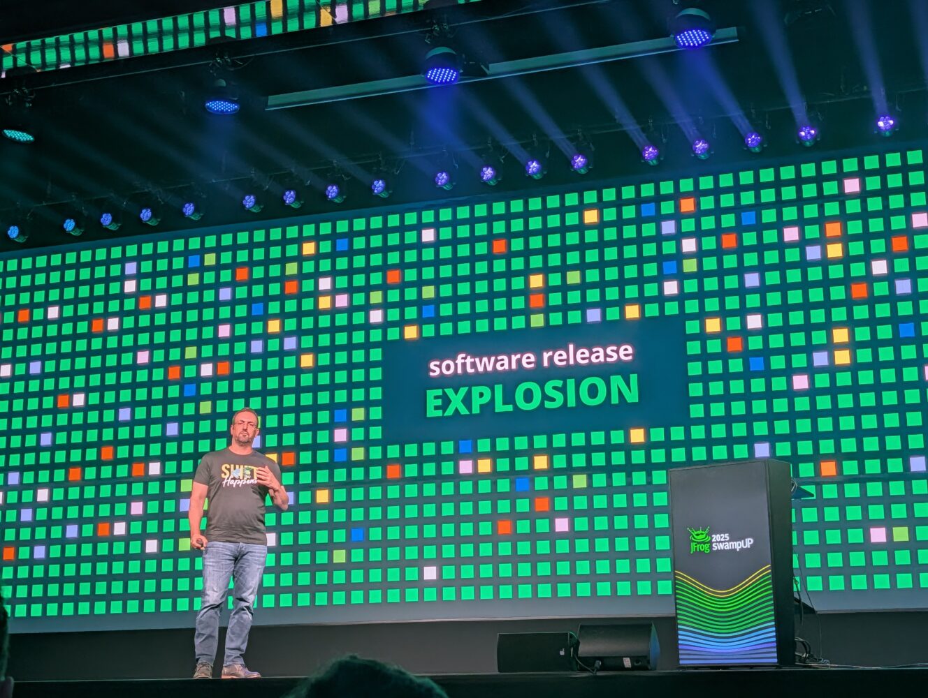 PXL_20251113_090220282.MP Een spreker staat op het podium voor een groot scherm met de tekst "software release EXPLOSION" op een technisch evenement.