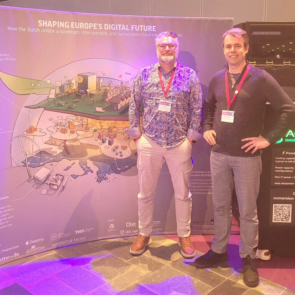 Twee mannen met conferentiebadges staan voor een kleurrijk scherm over het vormgeven van de digitale toekomst van Europa, met een illustratie van een digitale infrastructuur en verschillende partnerlogo's.