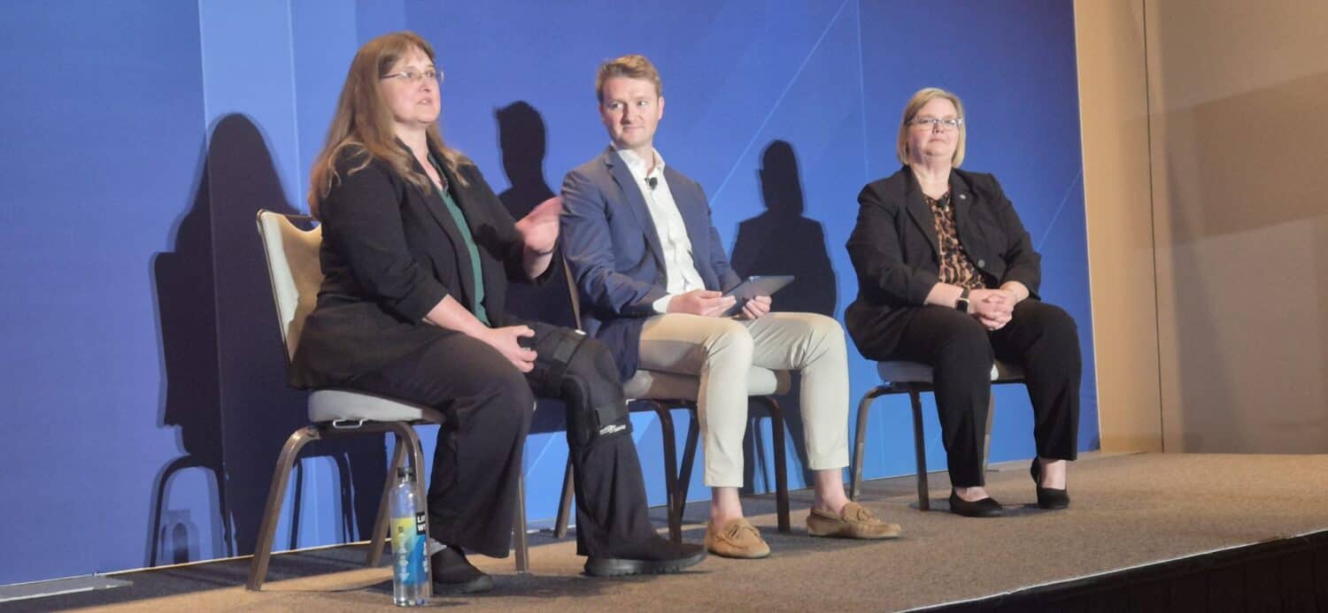 Drie mensen zitten op stoelen op een podium, verwikkeld in een paneldiscussie over Appian AI procesautomatisering. De achtergrond is blauw en één persoon spreekt terwijl de anderen aandachtig luisteren.