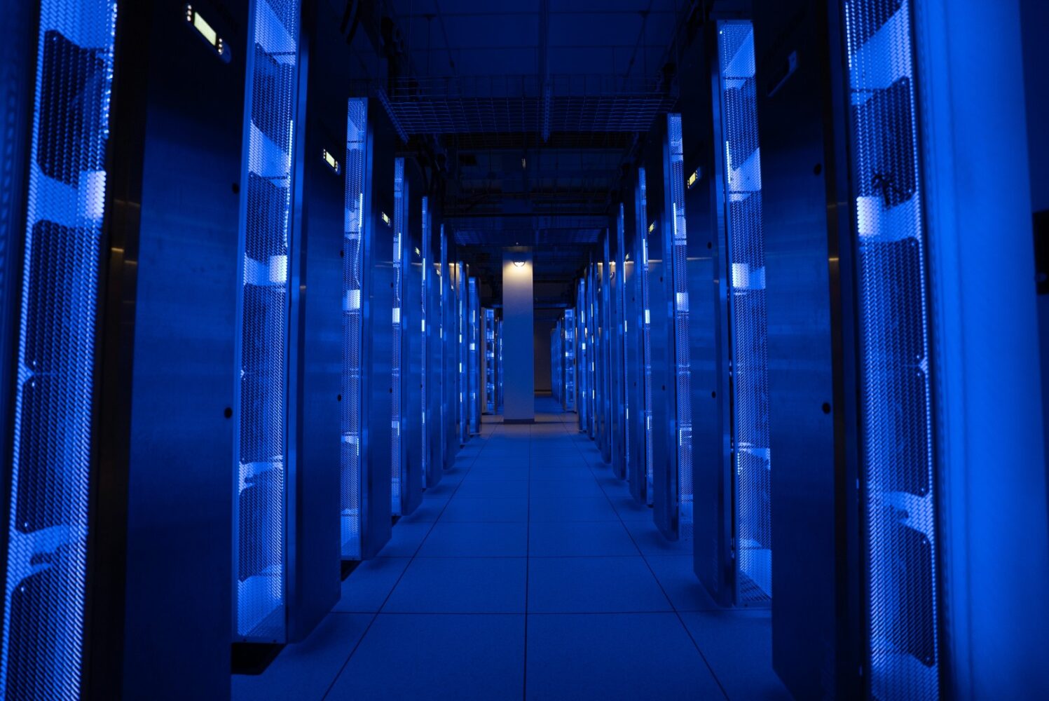 Een gangpad in een datacenter met rijen serverracks die worden verlicht door blauwe lampen, waardoor een symmetrische, hightech omgeving ontstaat.